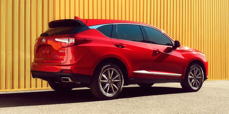 Red Acura SUV parked beside a bright yellow wall, shown from a rear three-quarter