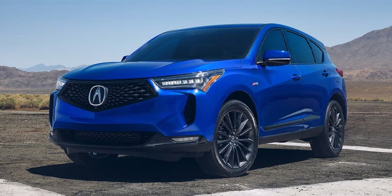 Blue Acura SUV parked on a paved surface with mountains and open sky in the background