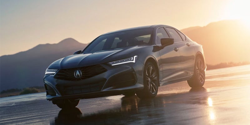 Dark Acura sedan parked on a reflective wet surface at sunset, shown from a front three-quarter angle
