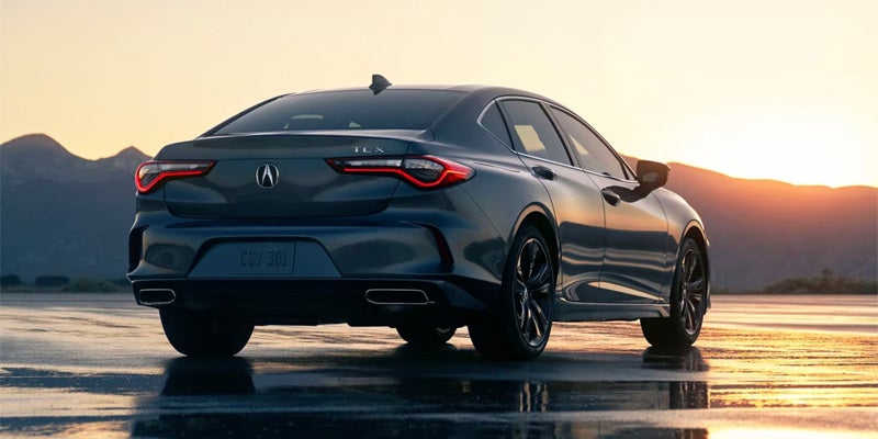 Rear three-quarter view of a dark Acura sedan on a reflective surface at sunset