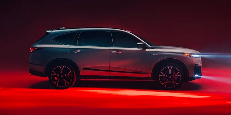 Side profile of a silver Acura MDX SUV in a studio setting with dramatic red lighting