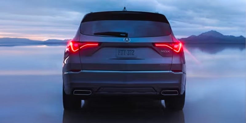 Rear view of a silver Acura MDX SUV with illuminated LED taillights, positioned on a reflective surface with mountains