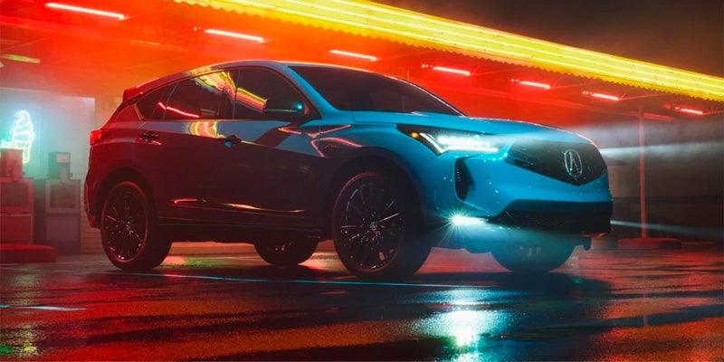 Acura SUV parked on a wet surface at night, illuminated by colorful neon lights reflected on the pavement