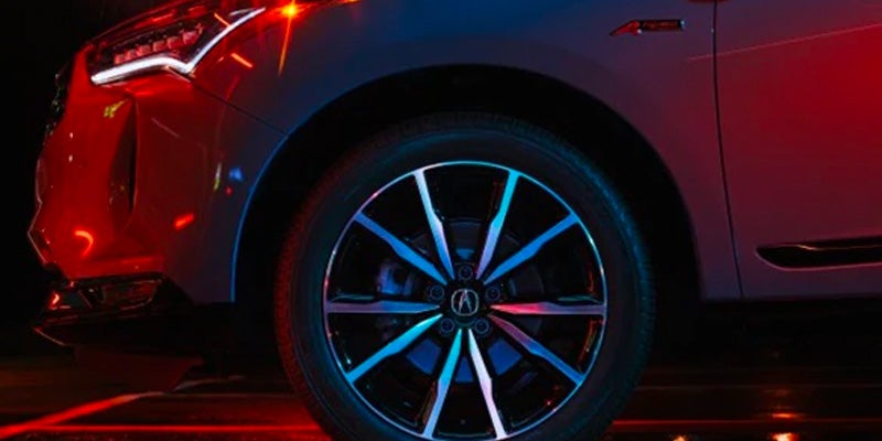 Close-up of an Acura SUV front wheel and lower body panel illuminated by red and blue lighting