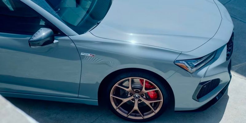 Close-up of an Acura sedan front wheel, brake caliper, and side body panel, highlighting performance styling details