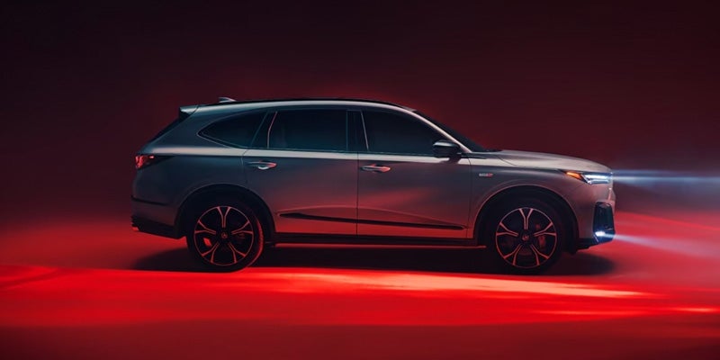 Side profile of a gray Acura SUV illuminated by red studio lighting against a dark background