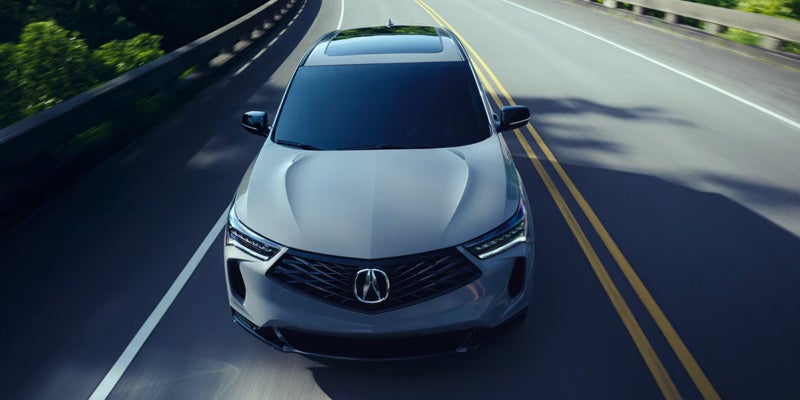 Gray Acura SUV driving on a multi-lane highway, viewed from a high angle looking down at its front.