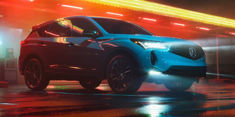 Blue Acura SUV parked on a wet surface at night, illuminated by colorful neon lights