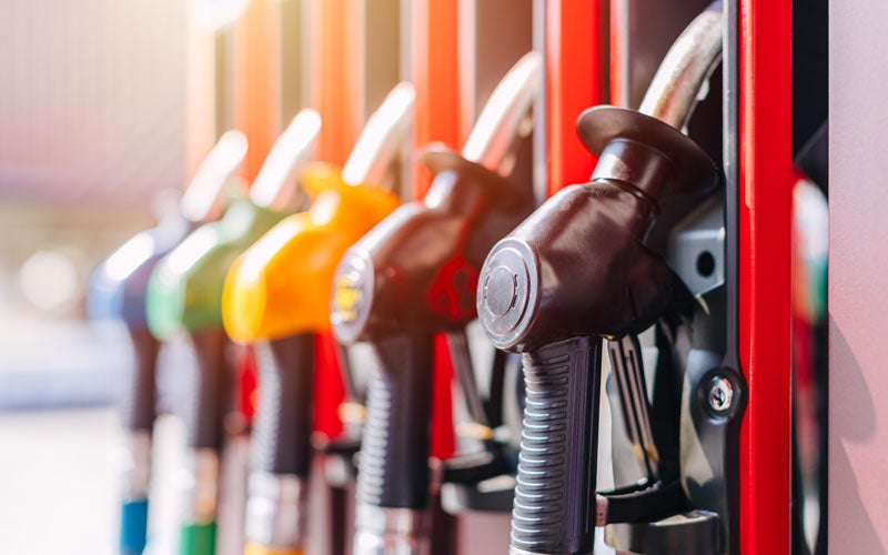 A close-up shot of several colorful gas pump nozzles lined up at a fuel station with a bright glare.